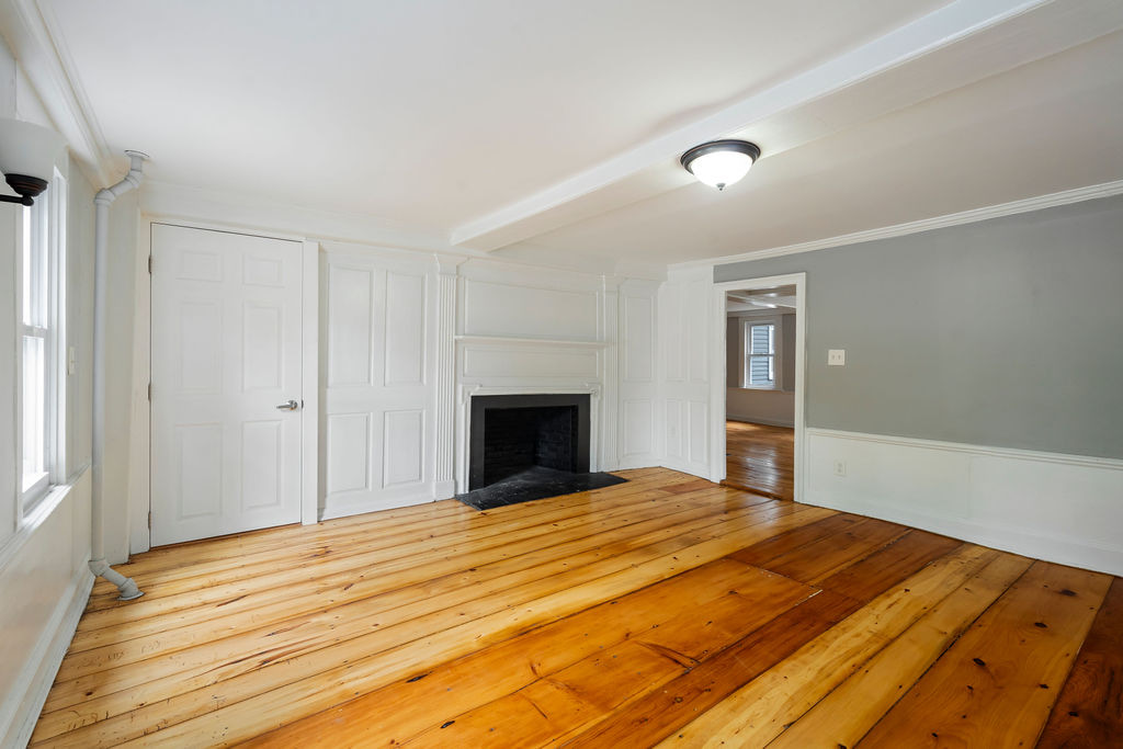 Empty room with wide wood floors, painted built-ins, and a traditional fireplace opening.